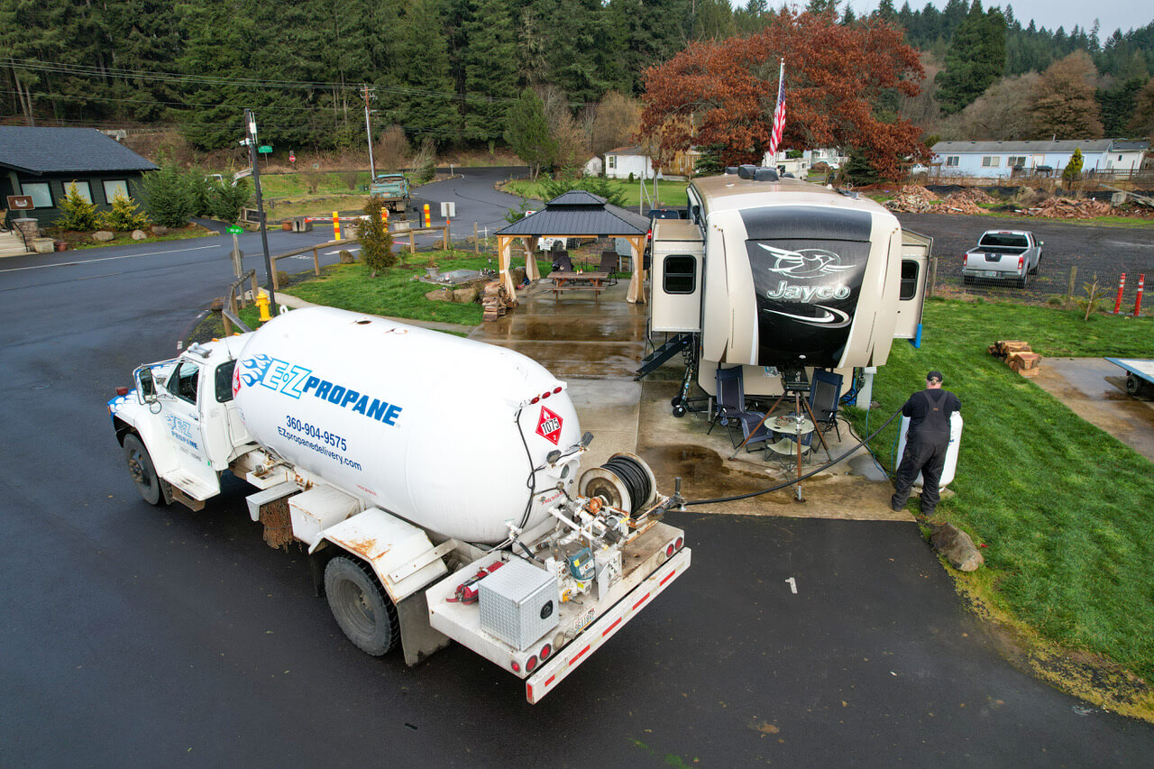 Large RV campground with rows of trailers and tents near a forest.